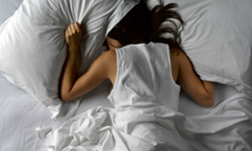 Mujer en la cama tapándose la cabeza con almohada
